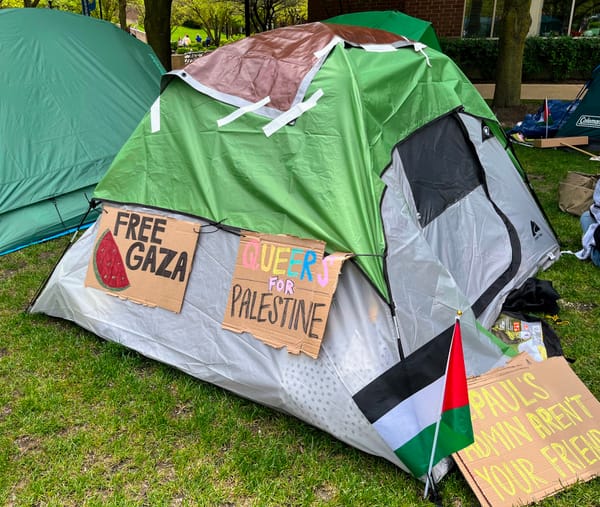 A tent bearing signs that say "Free Gaza" and "Queers for Palestine" has a Palestinian flag at its base.