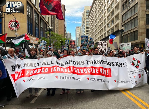 Palestine solidarity protesters block an intersection while holding a banner, signs and Palestinian flags.