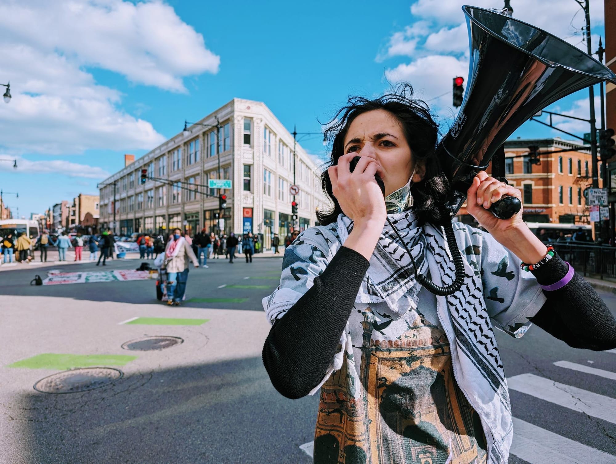 A protester wearing a keffiyeh speaks through a bullhorn in the street.