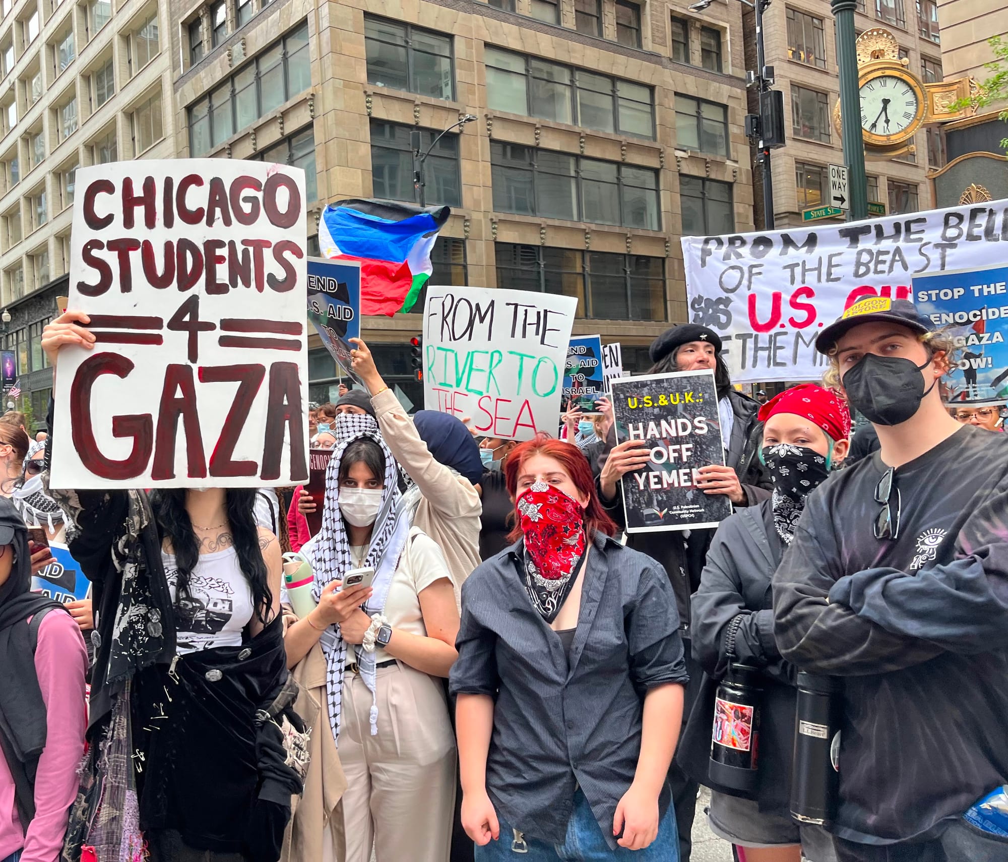 Masked protesters hold signs in the street. One reads, "Chicago students 4 Gaza."