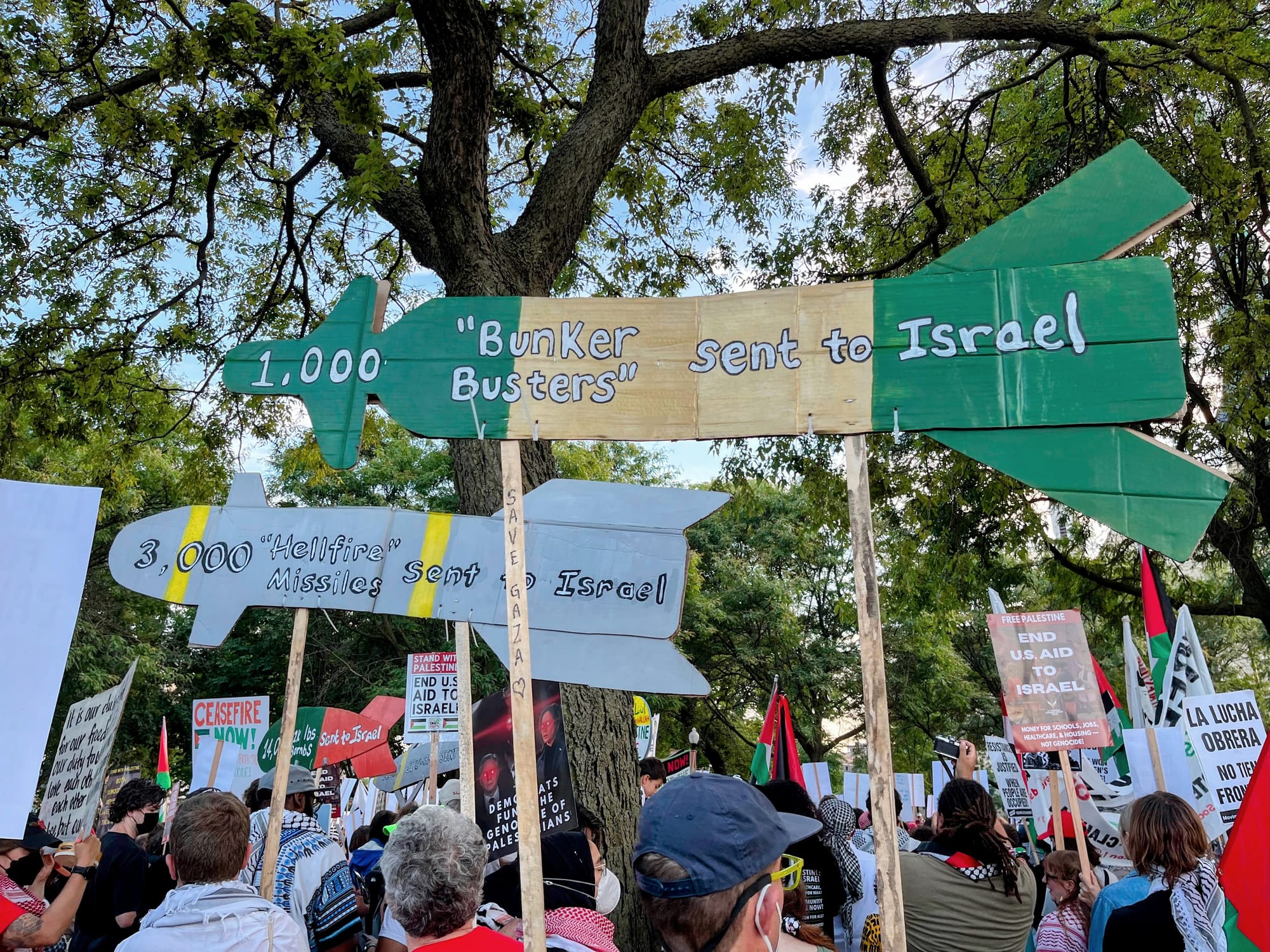 Two protest signs shaped like missiles are held at a protest. 