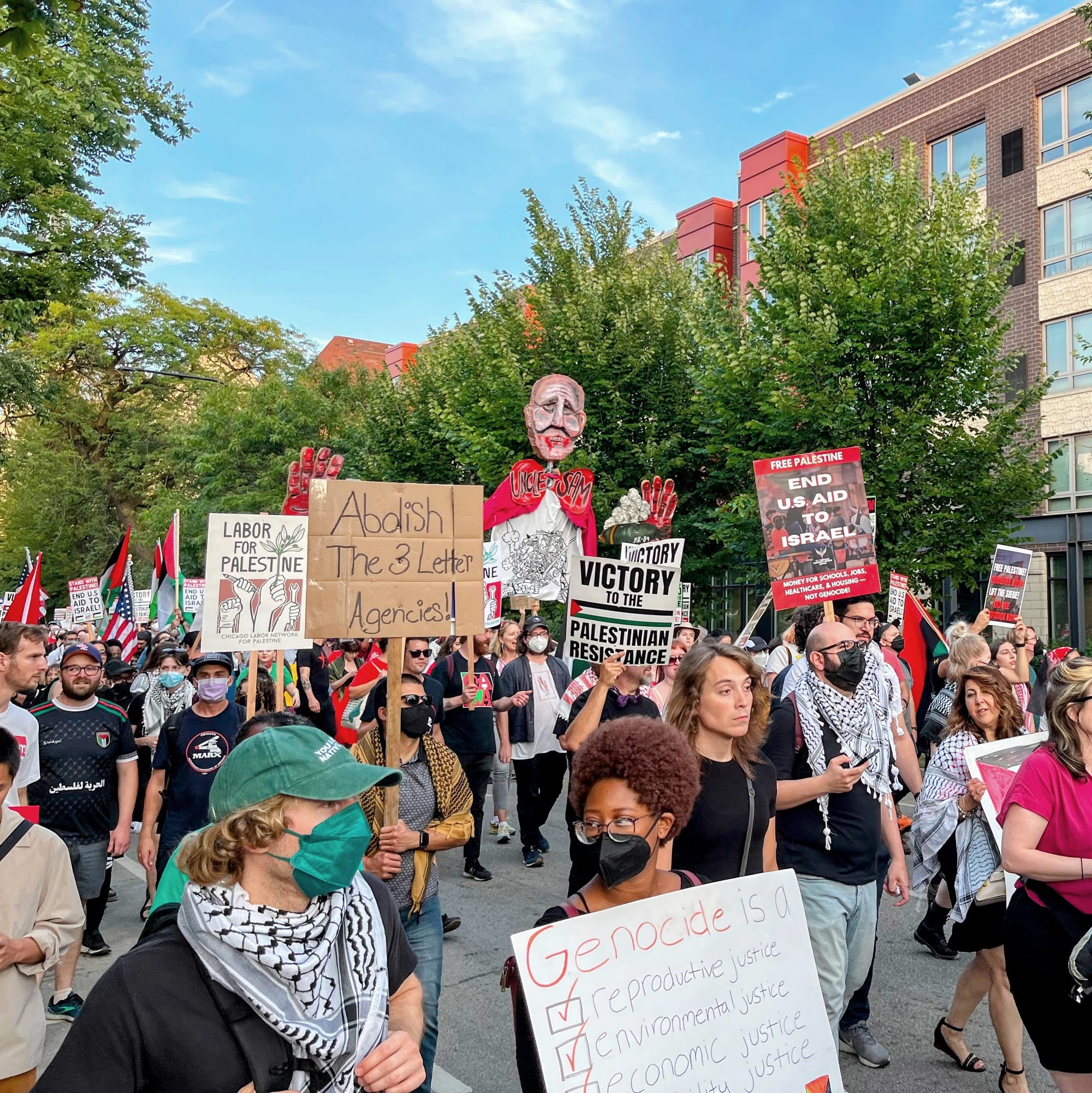 Palestine solidarity protesters carry signs and a puppet of a ghoulish Uncle Sam.