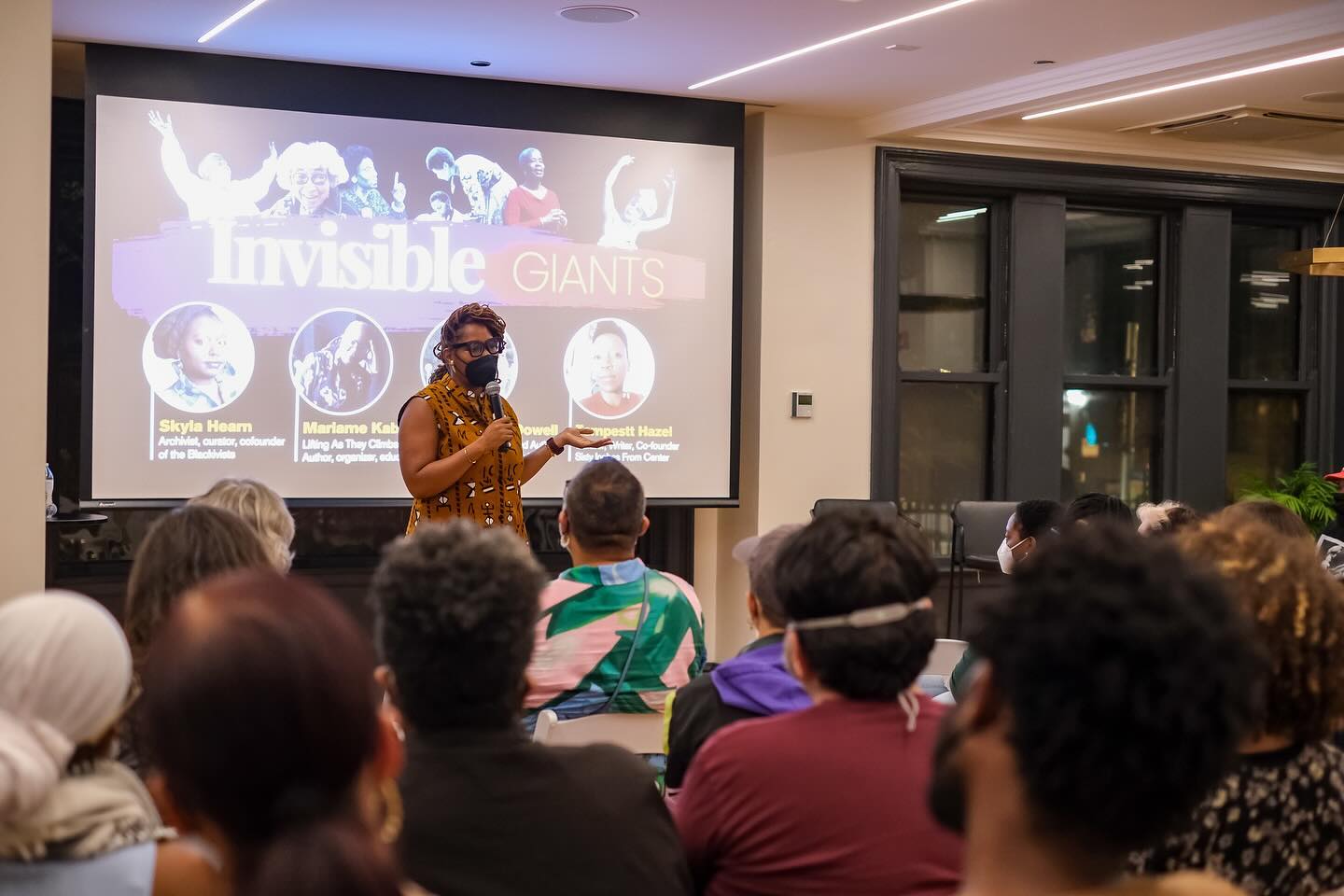 Essence McDowell addresses a crowd in front of a film screen.