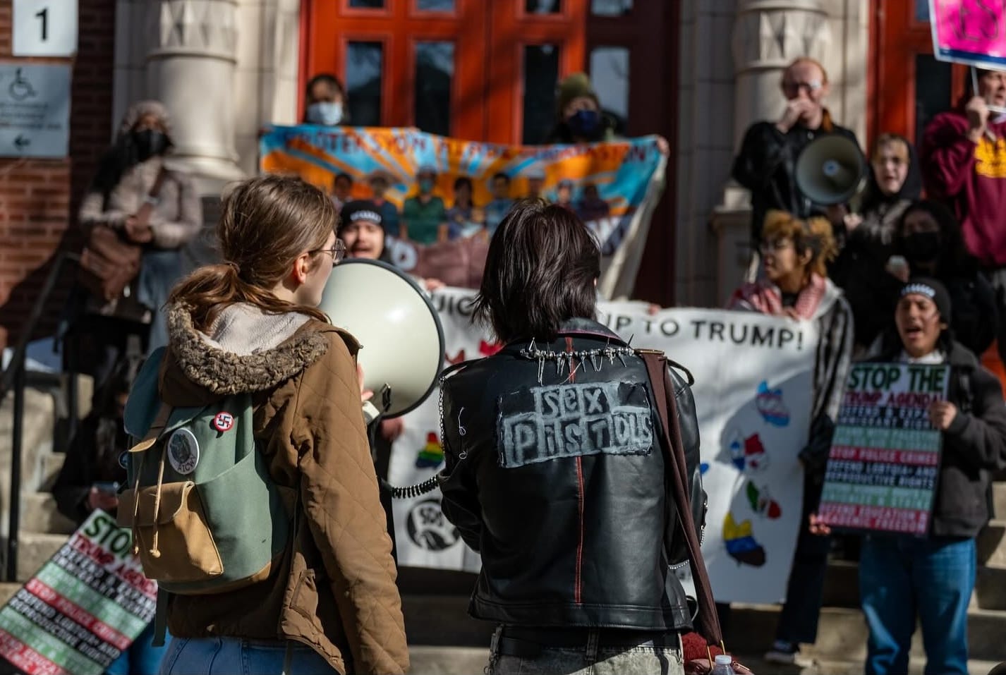 Students rally outside of a school. One speaks into a megaphone.