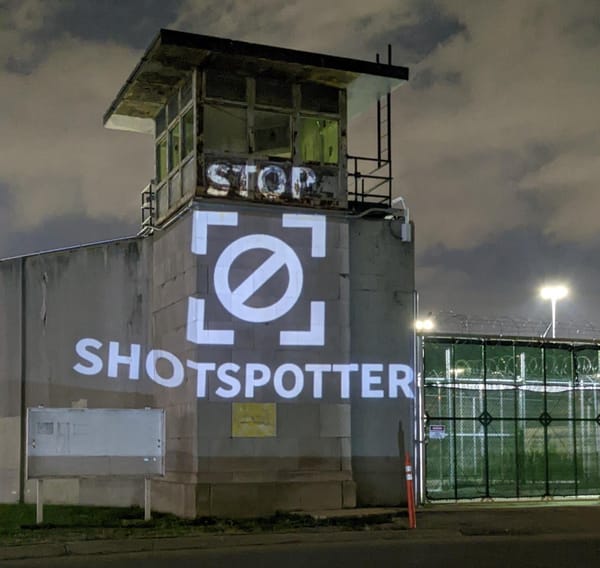 A large white graphic saying “Cancel Stop ShotSpotter” projected over a tall concrete tower at Cook County Jail in Chicago. 