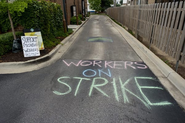 Chalked on a road are the words "Workers on Strike." A sign nearby says, "Support striking workers."
