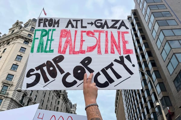 A hand holds up a sign that reads, "From ATL to Gaza, Free Palestine, Stop Cop City!"