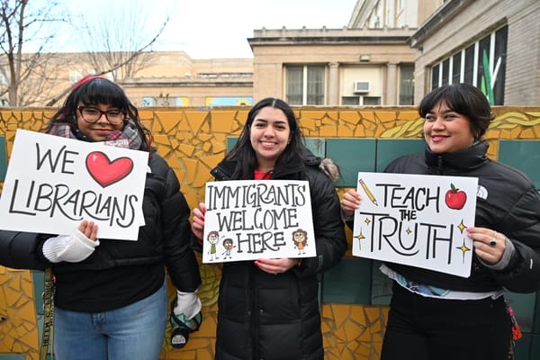 Three women hold signs with messages that include, "Immigrants welcome here."