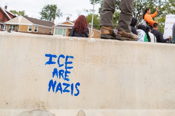 A protester stands on a cement barricade that bears graffiti that reads: "ICE are Nazis."